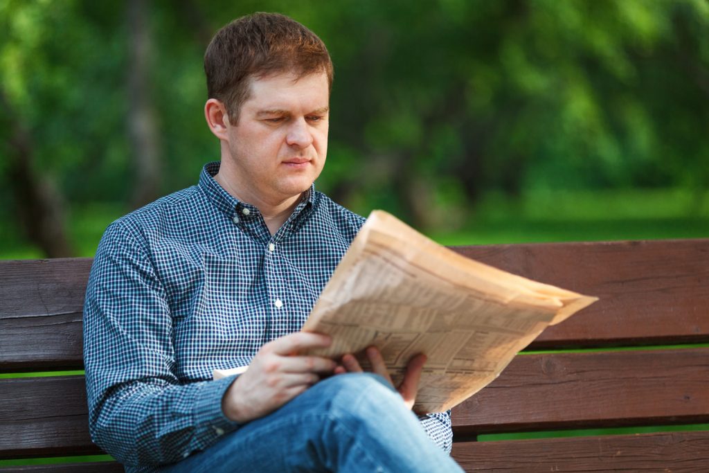Man reads newspaper on bench in the park Man reads a newspaper on a bench in the park
